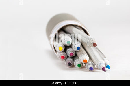 Matite colorate per uscire da una casella grigia su una superficie bianca. Foto Stock