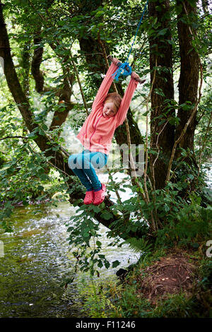 Ragazza avventurosa che gioca su un'oscillazione di corda in bosco vicino Il fiume Dart in Devon Foto Stock