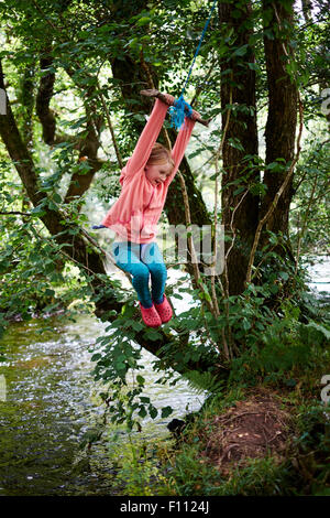 Ragazza avventurosa che gioca su un'oscillazione di corda in bosco vicino Il fiume Dart in Devon Foto Stock