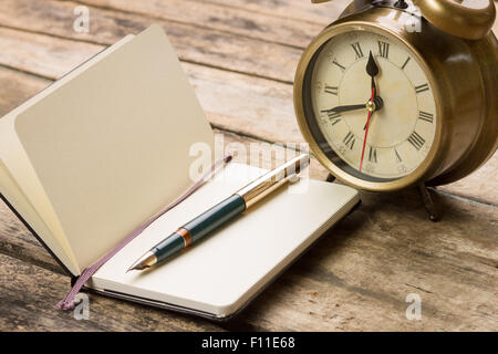 Aprire piccolo taccuino con penna stilografica e vecchia sveglia dietro. Colori caldi toni immagine vintage Foto Stock