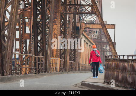 Donna che cammina da sola, veduta di una giovane donna vietnamita che indossa una maschera facciale che cammina attraverso il Long Bien Bridge in una giornata coperta e fumosa, Hanoi Vietnam Foto Stock