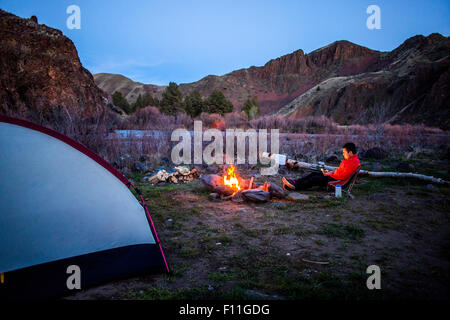 Escursionista caucasica seduti vicino al fuoco nel campo deserto, colline dipinte, Oregon, Stati Uniti Foto Stock
