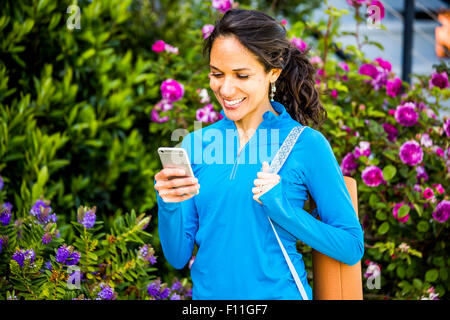 Donna ispanica utilizzando il cellulare in giardino Foto Stock