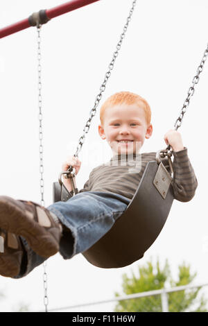 Caucasian ragazzo seduto sul parco giochi swing Foto Stock