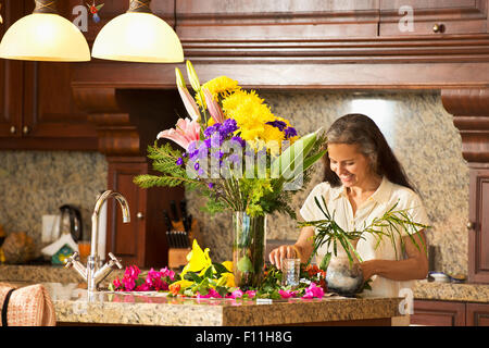 Donna ispanica disponendo dei fiori in cucina Foto Stock