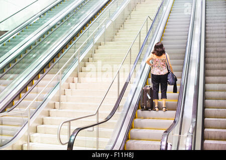 Donna ispanica permanente sulla escalator Foto Stock