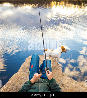 Uomo caucasico la pesca con il cane nel lago in remoto