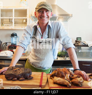 Uomo sorridente con arrosti di carne in cucina Foto Stock