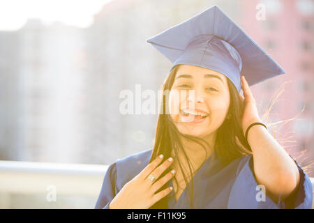 Sorridente ragazza ispanica graduazione da indossare accappatoio e mortarboard Foto Stock