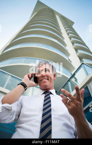 Basso angolo vista di imprenditore caucasico tramite telefono cellulare a un alto edificio Foto Stock