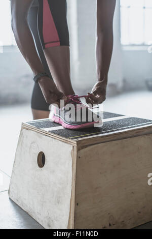 Atleta legando le sue scarpe su piattaforma in palestra Foto Stock