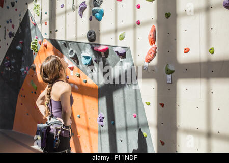 Atleta esaminando parete di roccia in palestra Foto Stock