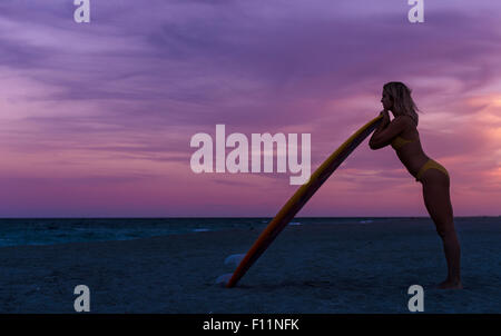 La donna caucasica appoggiata sulla tavola da surf in spiaggia Foto Stock