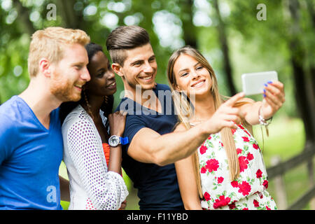 Un gruppo di giovani e coppie tenendo selfies nella natura e sorridente Foto Stock