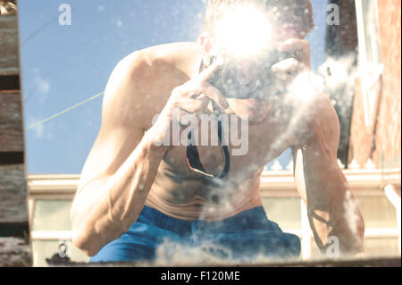 Ma povero uomo muscolare con la sua parte superiore a scattare foto di se stesso in uno specchio. Abstract scatti. Lo specchio è la posa sull'erba. Foto Stock