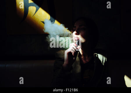 La ragazza si siede e fuma sigaretta elettronica Foto Stock