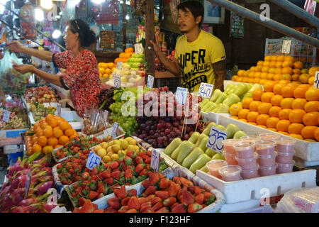 Pressione di stallo di frutta in una Bangkok mercato alimentare con prezzi in baht tailandese e una donna che serve i clienti, Thailandia Foto Stock