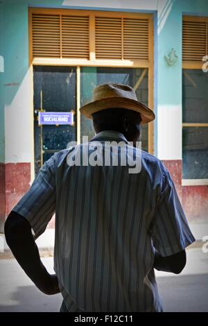 Vista posteriore del locale uomo nel cappello di Panama e camicia a righe, il rilevamento della strada dall'ombra di un negozio porta, Havana, Cuba Foto Stock