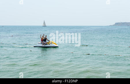 Coppia giovane sventolare da un jet ski mid ocean come essi godere un po' di acqua a scopo ricreativo sport sulle loro vacanze estive Foto Stock