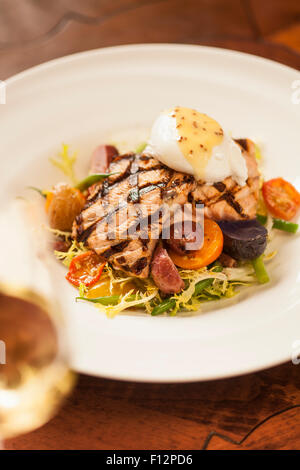 Grigliata di salmone king con insalata frisee, pancetta, soft Uovo affogato e vinaigrette di senape e un bicchiere di chardonnay Foto Stock