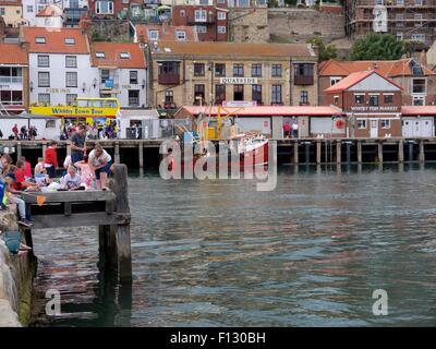 La gente la pesca del granchio in Whitby con il tour bus passando in background Foto Stock