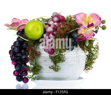 Composizione colorata fatta di fiori artificiali e di frutti in un vecchio vaso di vetro isolato su sfondo bianco. Foto Stock