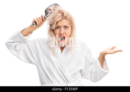 Orinato giovane donna in un accappatoio bianco con i suoi capelli aggrovigliato in una spazzola per capelli isolati su sfondo bianco Foto Stock