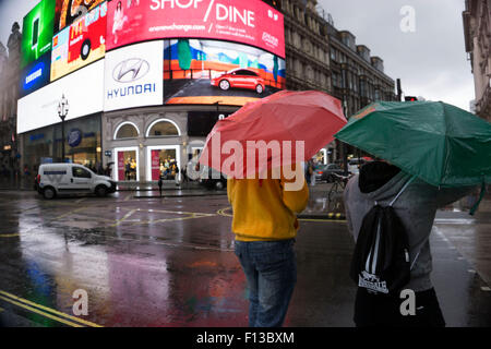 Londra, Regno Unito. Domenica 23 agosto 2015. Estate Pesanti rovesci di pioggia nel West End. Popolo coraggioso il tempo umido armati con ombrelloni e indumenti impermeabili. Piccadilly Circus. Foto Stock