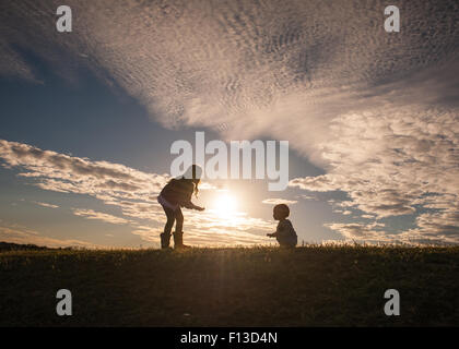 Silhouette di una ragazza con un bambino ad imparare a camminare Foto Stock