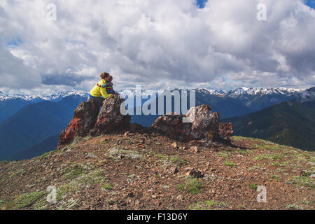 Madre seduta su una roccia sulla montagna che abbraccia il suo figlio Foto Stock