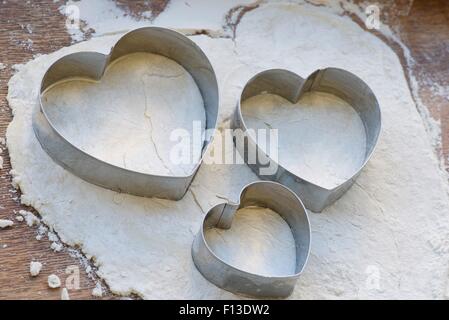 Tre a forma di cuore frese di pasticceria su un rotolò fuori banda di pasta Foto Stock