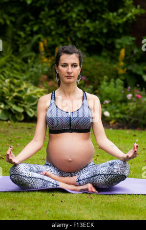 Donna incinta a praticare yoga in giardino Foto Stock