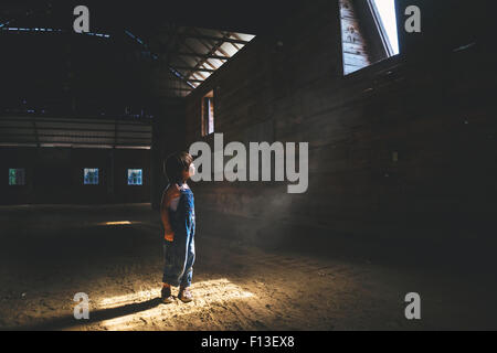 Ragazzo che guarda fino in corrispondenza di una finestra in un granaio Foto Stock