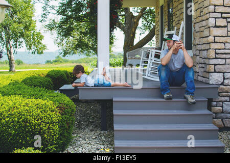 Uomo seduto sul portico passi guardando il figlio Foto Stock