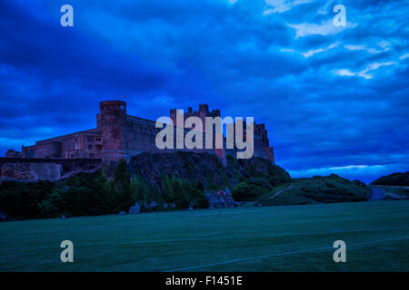 In tarda serata la vista del tramonto di Bamburgh Castle in Northumberland con un molto burrascoso sky e una tinta rossa sulle pareti del castello. Foto Stock