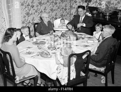 Anni Cinquanta tre generazioni la famiglia avente per la festa del Ringraziamento pasto NELLA SALA DA PRANZO PADRE CARVING TURCHIA Foto Stock