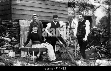 1890s tre uomini una donna di casa capannone guardando la fotocamera di un solo uomo il taglio di legna da ardere tronchi con sega a telaio Foto Stock