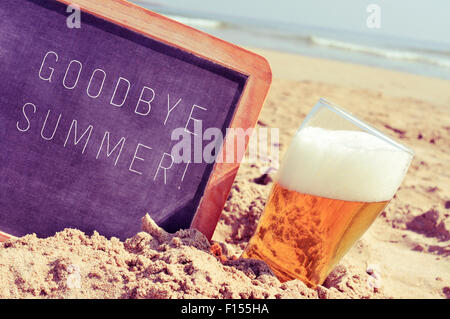 Primo piano di una lavagna con il testo addio estate scritto in esso e un bicchiere di birra, sulla sabbia di una spiaggia Foto Stock