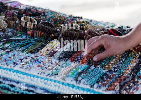 Un uomo raggiunge a prelevare un braccialetto bordato da una tabella di gioielli fatti a mano in un mercato di spiaggia in Belize. Foto Stock