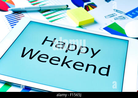 Il testo Happy Weekend sullo schermo di un tablet, collocato su un tavolo pieno di grafici Foto Stock