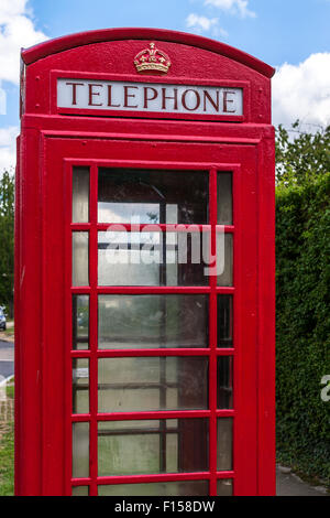 Unico British telefono rosso box o stand contro un Cielo di estate blu in una posizione suburbana Foto Stock