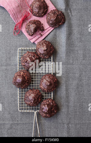 Cioccolato, amaretti di cocco i cookie su una griglia di raffreddamento con una rosa e un panno assorbente e lo spago, studio shot su sfondo grigio Foto Stock