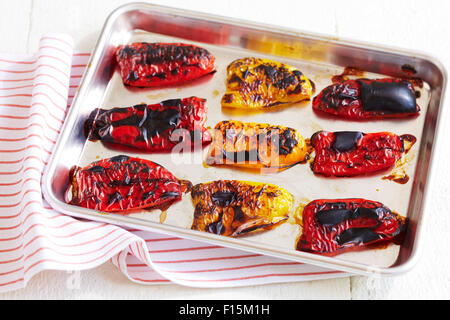 Arrosto di giallo e peperoni rossi su una teglia da forno con un rosso striato igienico, studio shot su sfondo bianco Foto Stock