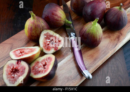 Fichi freschi sul tagliere di legno con coltello su un legno scuro in stile vintage tabella. Foto Stock