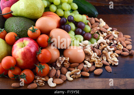 Alimentazione sana con frutta fresca, mele, pere, avocadi, uva, uova, frutta secca, pomodori cetrioli su un legno rustico sfondo. Foto Stock