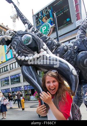 Toronto, Canada. Il 27 agosto, 2015. Un turista interagisce con un busker dai Paesi Bassi svolge un costume stilt presentano un 18 piedi di altezza dinosauro durante il 2015 Internazionale di Toronto a BuskerFest Yonge-Dundas Square a Toronto, Canada, 27 agosto 2015. I quattro giorni del festival ha dato dei calci a fuori il giovedì. Credito: Zou Zheng/Xinhua/Alamy Live News Foto Stock