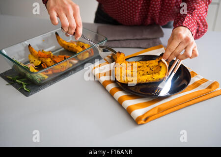 Un elegante donna mani di servizio sono una fetta di zucca arrosto su di una piastra di scuro. Il tè-asciugamano sotto la piastra porta la Foto Stock