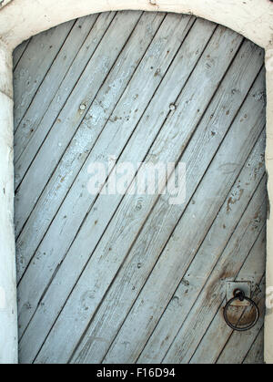 La porta delle tavole di legno sulla diagonale con una sommità semicircolare e anello di ferro arrugginito Foto Stock