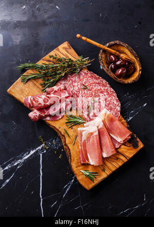 Fette di prosciutto di Parma su tavola di legno con salame e rosmarino nero su sfondo marmo Foto Stock