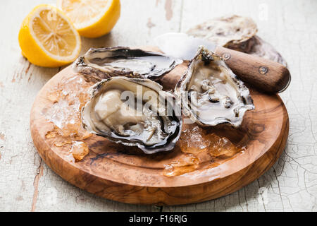 Apre Ostriche di olive wood board sul blu sullo sfondo di legno con limone e coltello oyster Foto Stock